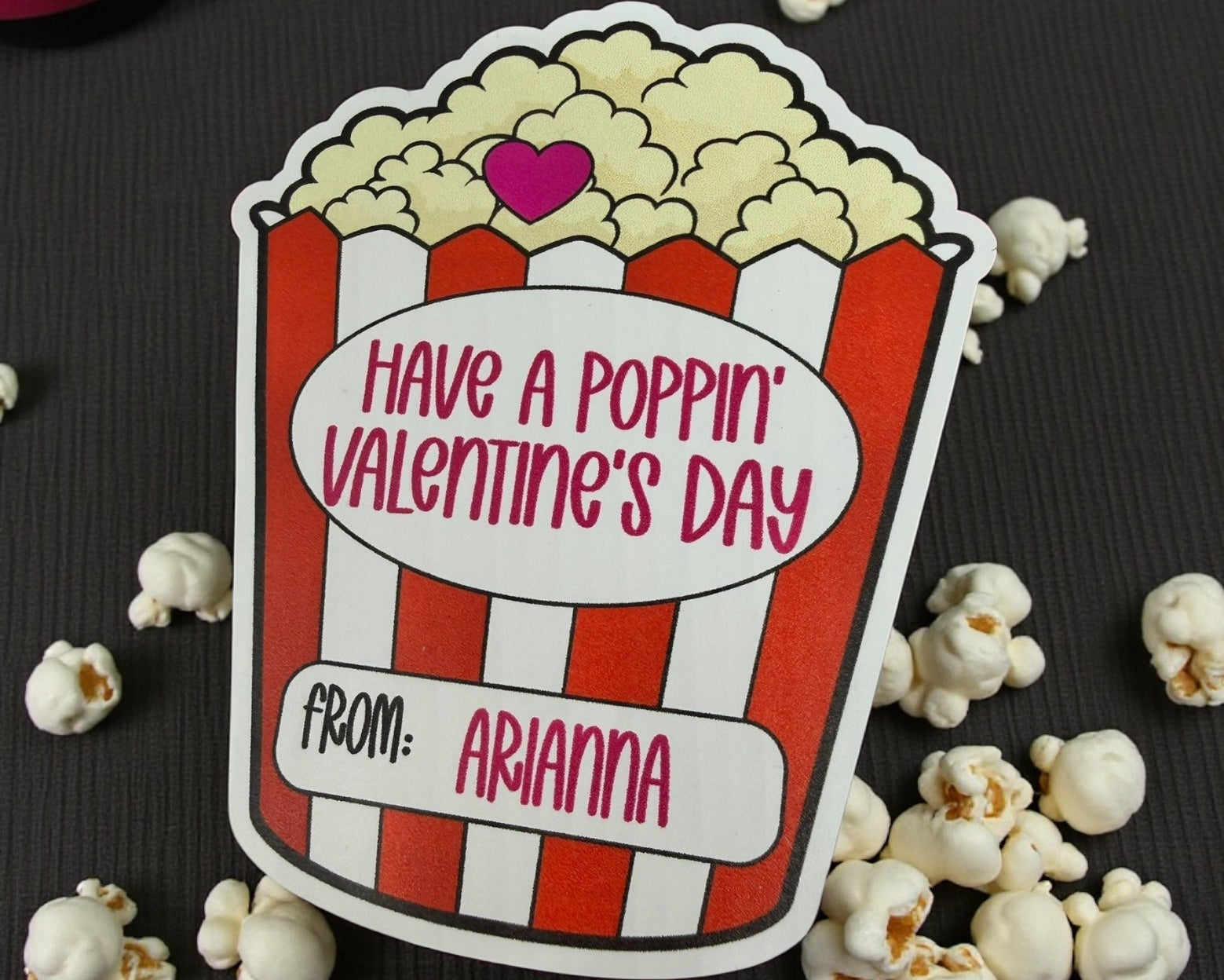 Valentine's Day card with popcorn design and text 'Have a poppin' Valentine's Day from Arianna' surrounded by popcorn on a dark surface.
