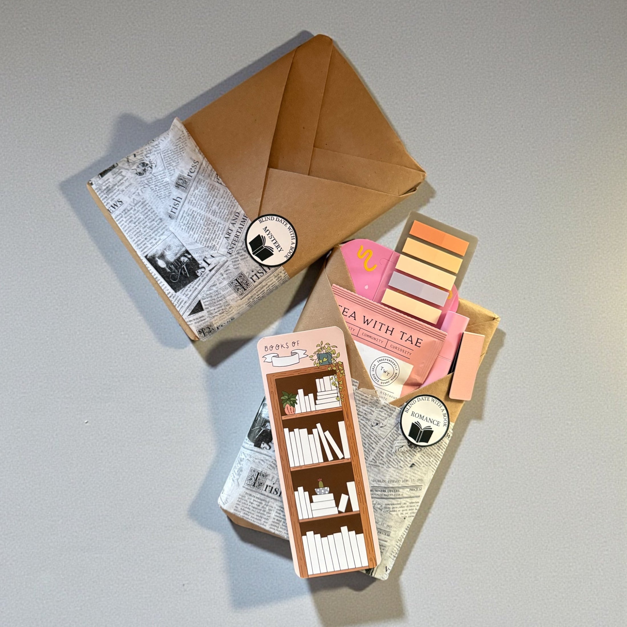 Set of stationery items including a small book, tea packaging, and colorful notepads on a gray surface.